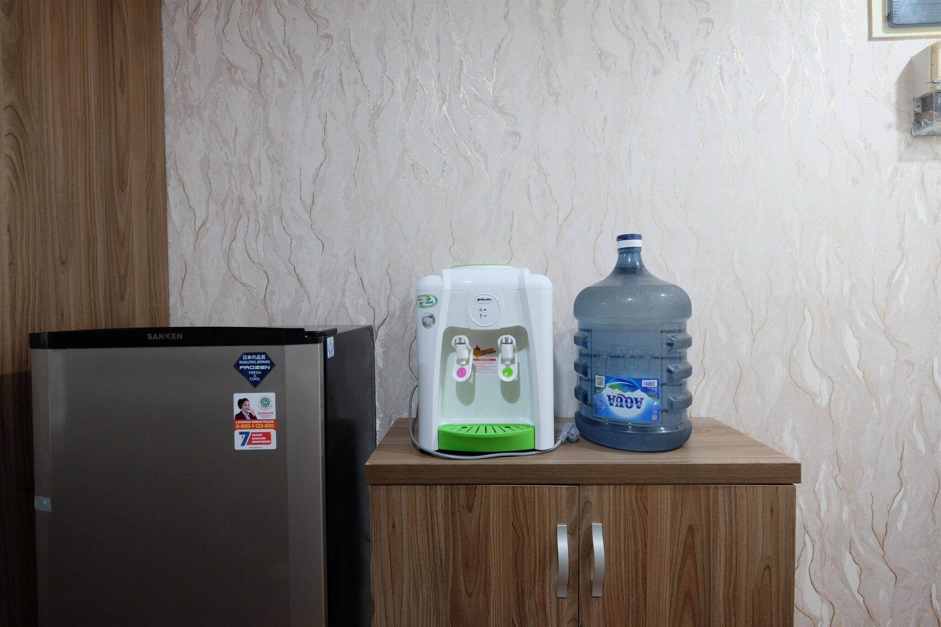 A refrigerator, a water dispenser, and a large water bottle on a wooden counter.