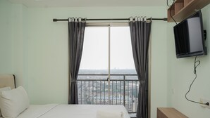 Habitación de hotel con cama, televisión, ventana con cortinas y vista a la ciudad.
