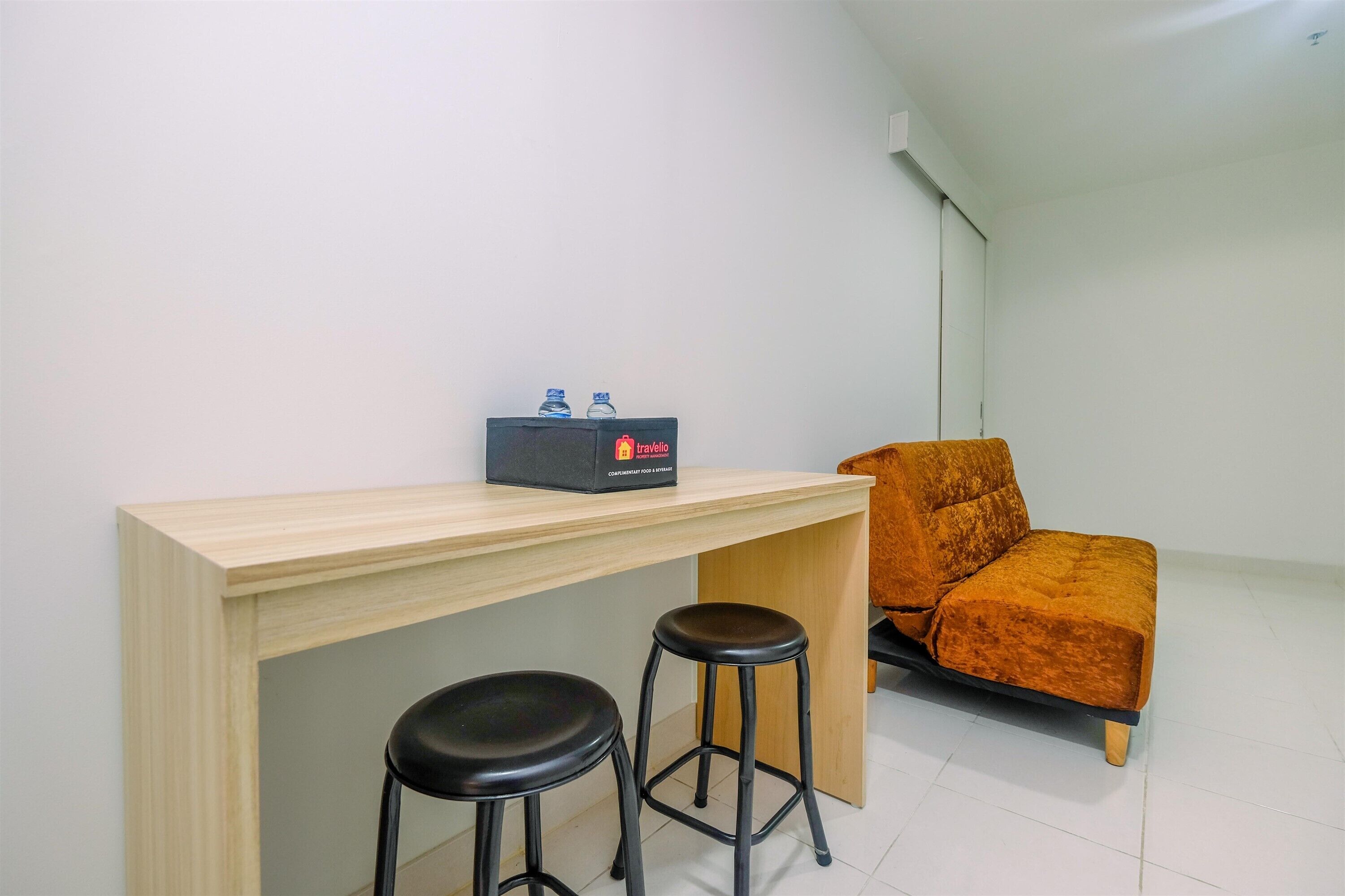 A small, modern room with a wooden desk, two black stools, and a single orange sofa.