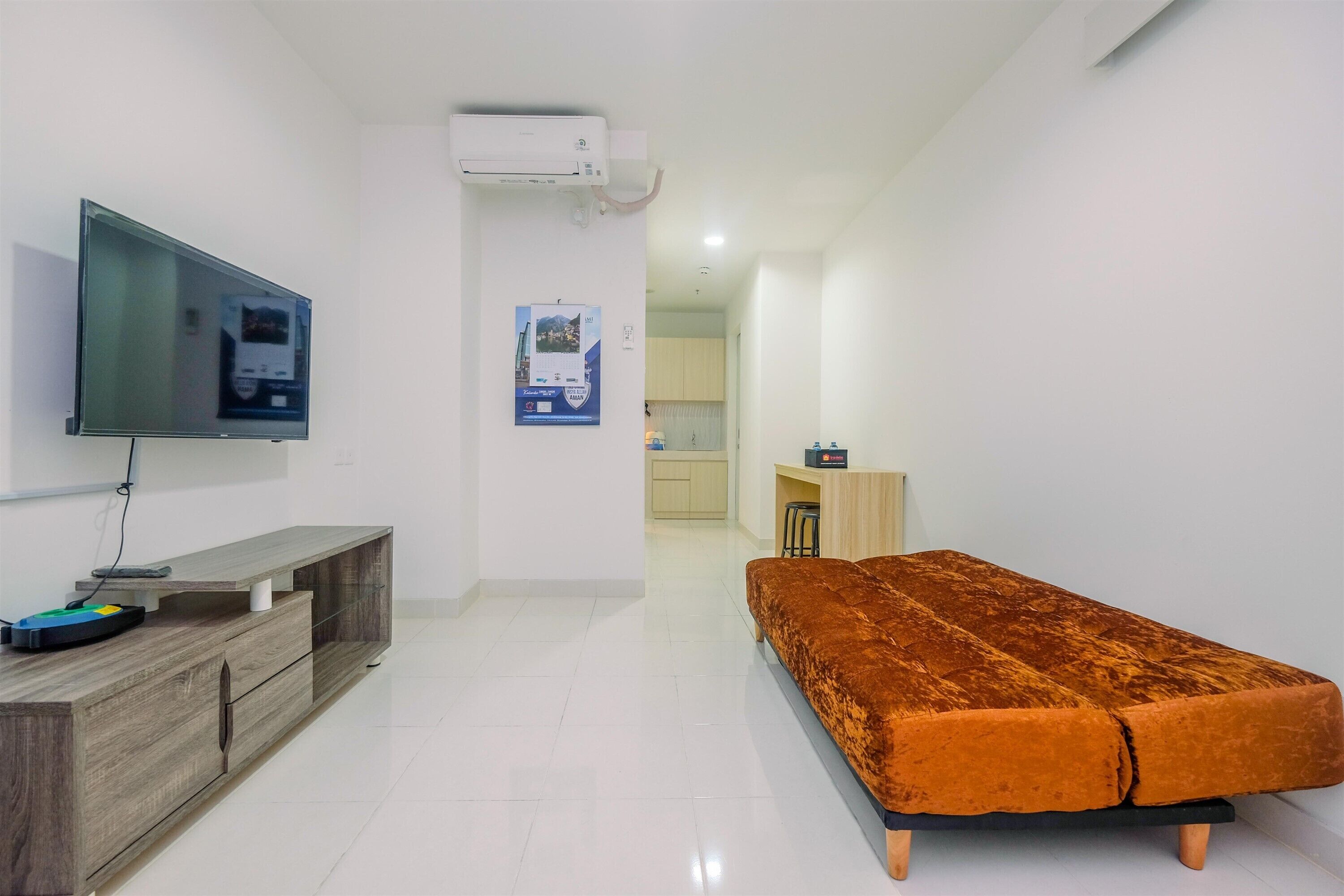 A modern living room with a flat-screen TV, wooden console, and a plush orange sofa.