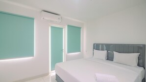 A hotel room with a large bed, white walls, teal-colored doors, and a ceiling air conditioner.