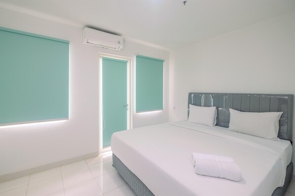 A hotel room with a large bed, white walls, teal-colored doors, and a ceiling air conditioner.