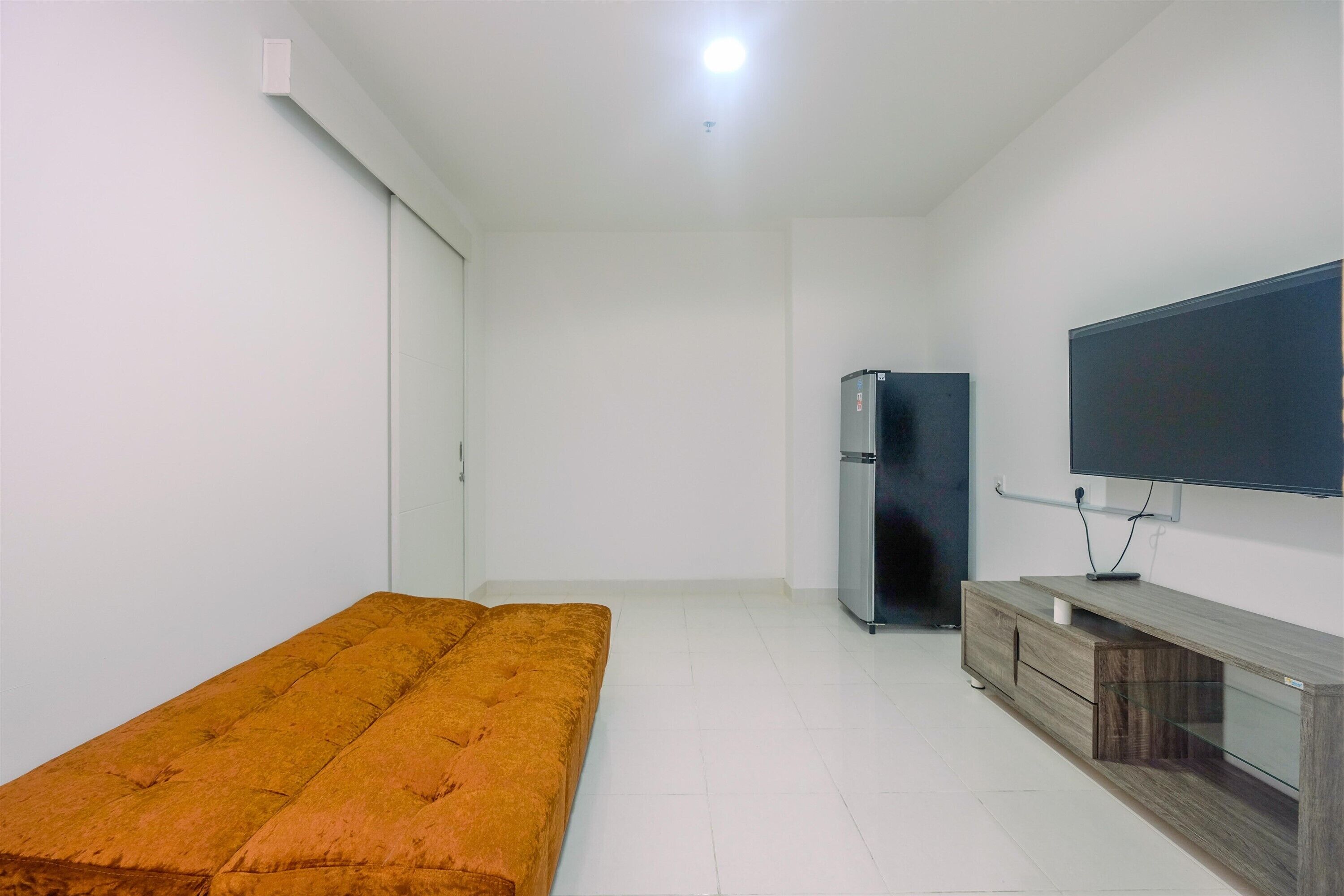 Una habitación con una cama individual, un televisor fijado a la pared, un armario de madera y un refrigerador.