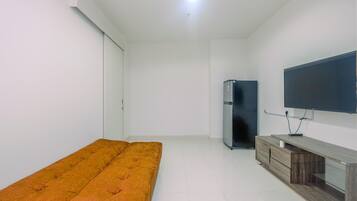 Una habitación con una cama individual, un televisor fijado a la pared, un armario de madera y un refrigerador.