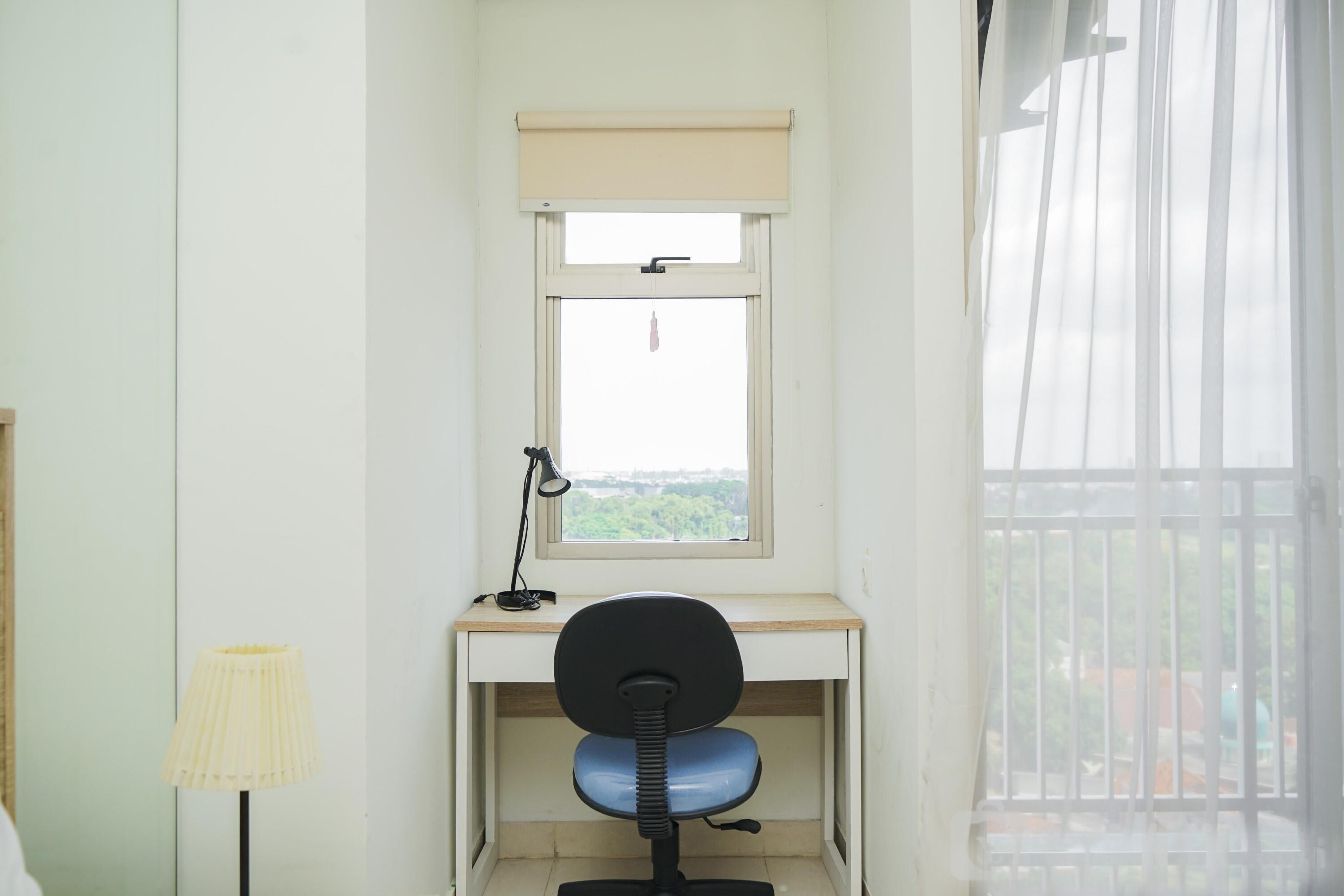 Une petite pièce comprenant un bureau, une chaise, une lampe et une fenêtre donnant sur un paysage verdoyant.