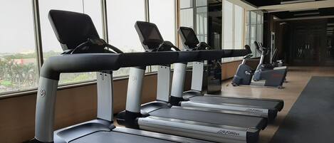 A row of treadmills in a gym with large windows and a view of the city.
