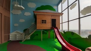 Un espace de jeux avec un toboggan, une cabane en bois et une vue dégagée grâce à de grandes fenêtres.