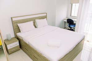 A neatly made bed with white linens, a wooden headboard, and a bedside table with a lamp and a small box. - Comfort and Tidy Studio Apartment Springwood Residence Tangerang (Tangerang)