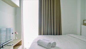 A hotel room with a bed, a TV, a desk, and a window with curtains. - Scenic and Strategic Studio Apartment at Springwood Residence (Tangerang)