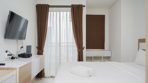 A hotel room with a bed, a desk with a flat-screen TV, a desk lamp, and a window with curtains. - Cozy Studio Apartment at Springwood Residence Tangerang (Tangerang)