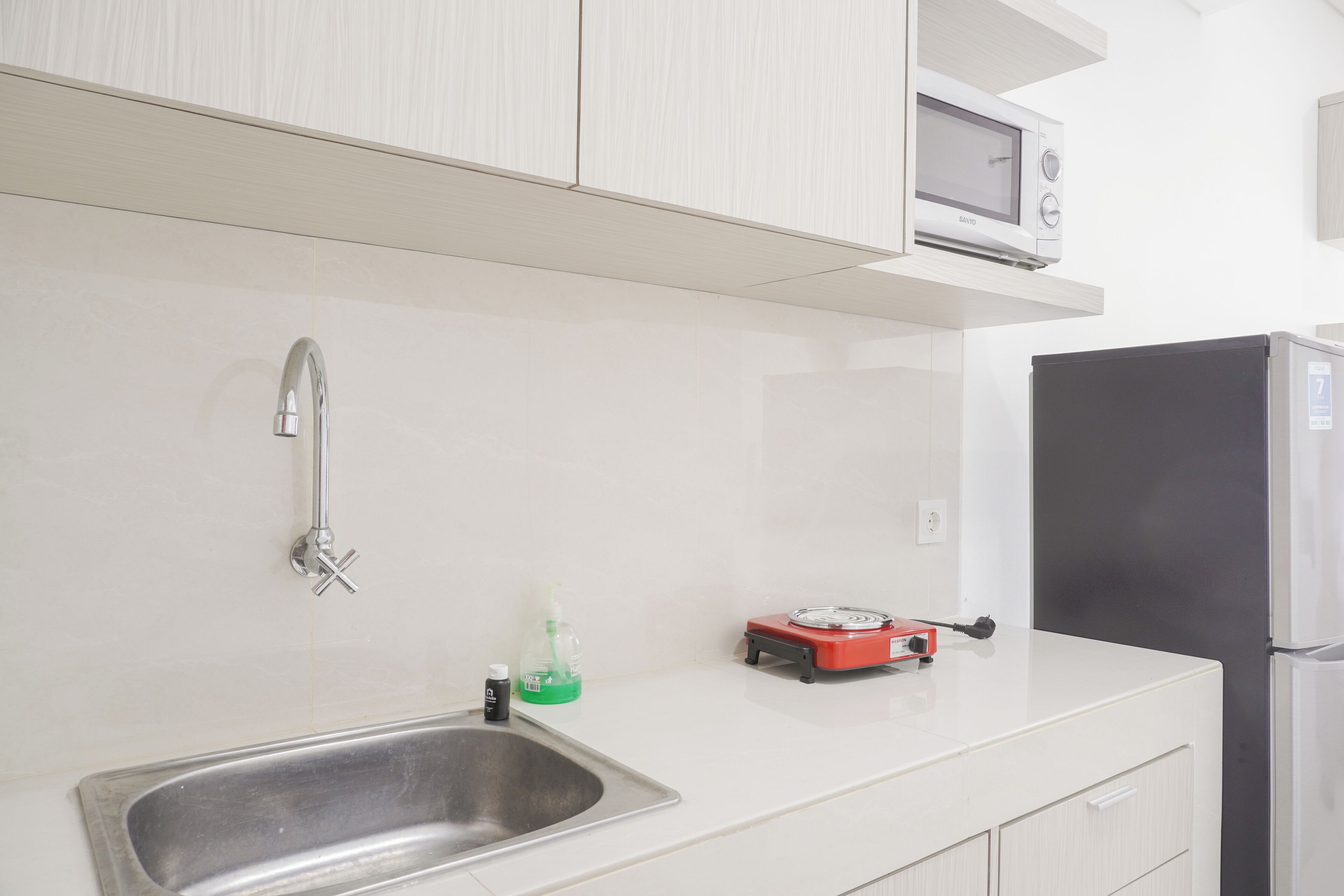 A kitchen with a stainless steel sink, a microwave, a red electric kettle, and a black refrigerator.