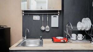 A kitchen with a sink, a red electric stove, hanging utensils, and a dish rack with white mugs. - Comfy and Modern Studio at Serpong Greenview Apartment (South Tangerang)