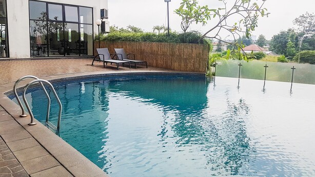 An outdoor swimming pool with a wooden deck, two lounge chairs, and a metal pool ladder. - Comfy and Modern Studio at Serpong Greenview Apartment (South Tangerang)