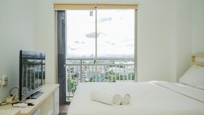 A hotel room with a bed, a TV on a desk, and a view of a cityscape through a large window. - Cozy Living Studio Apartment Springwood Residence near IKEA Alsut (Tangerang)