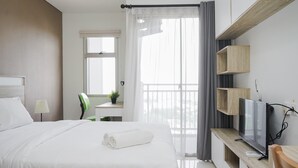 A modern hotel room with a large bed, a TV on a wooden console, a window with curtains, and a small desk with a chair. - Homey Studio Apartment Springwood Residence (Tangerang)