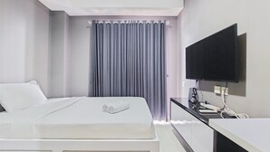 A hotel room with a bed, a flat-screen TV mounted on the wall, and a desk with a computer and other items. - Luxury Studio at Springwood Residence Tangerang Apartment (Tangerang)