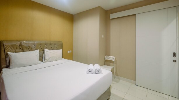 A hotel room with a bed, pillows, a chair, and a wardrobe. - Strategic Studio at Sentul Tower Apartment (Citaringgul)