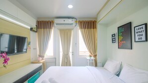 A hotel room with a bed, a TV, a desk, and a window with curtains. - New Furnished Studio at Sentul Tower Apartment (Citaringgul)