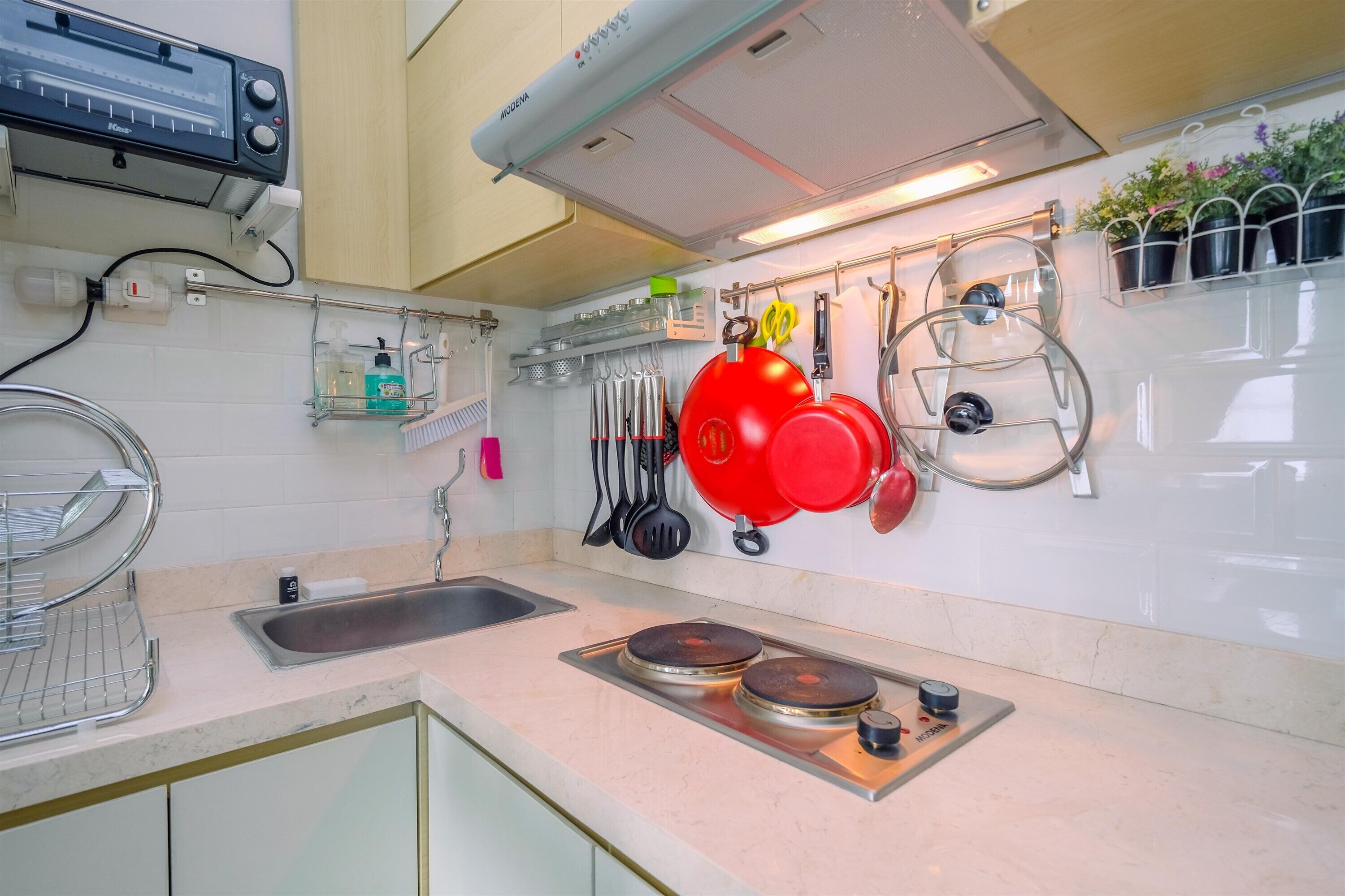 A kitchen with a built-in stove, a sink, and a wall-mounted pot rack with red pots.