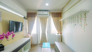 A hotel room with a flat-screen TV, a bench, a small table, and a wall with decorative elements. - New Furnished Studio at Sentul Tower Apartment (Citaringgul)