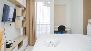 Quarto de hotel com cama, escrivaninha, televisão e janela com cortinas.
