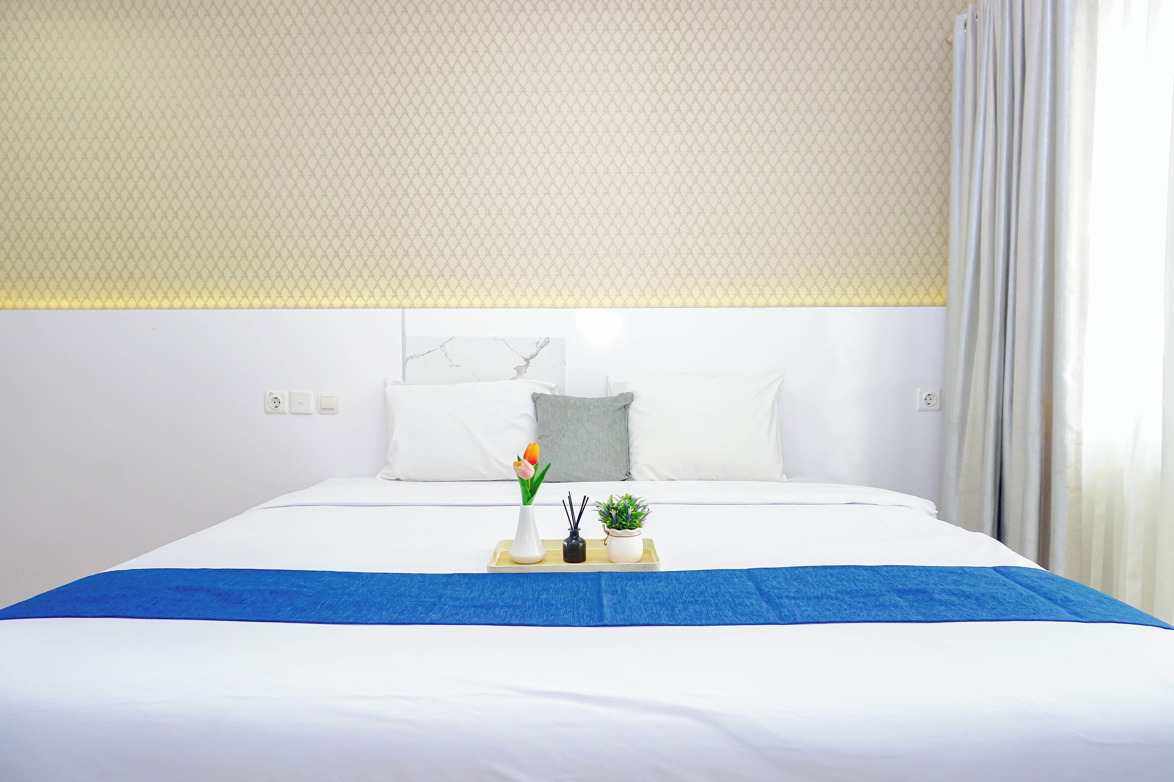 A neatly made bed with a blue bedspread, white pillows, and a tray with a vase of flowers and a small plant.