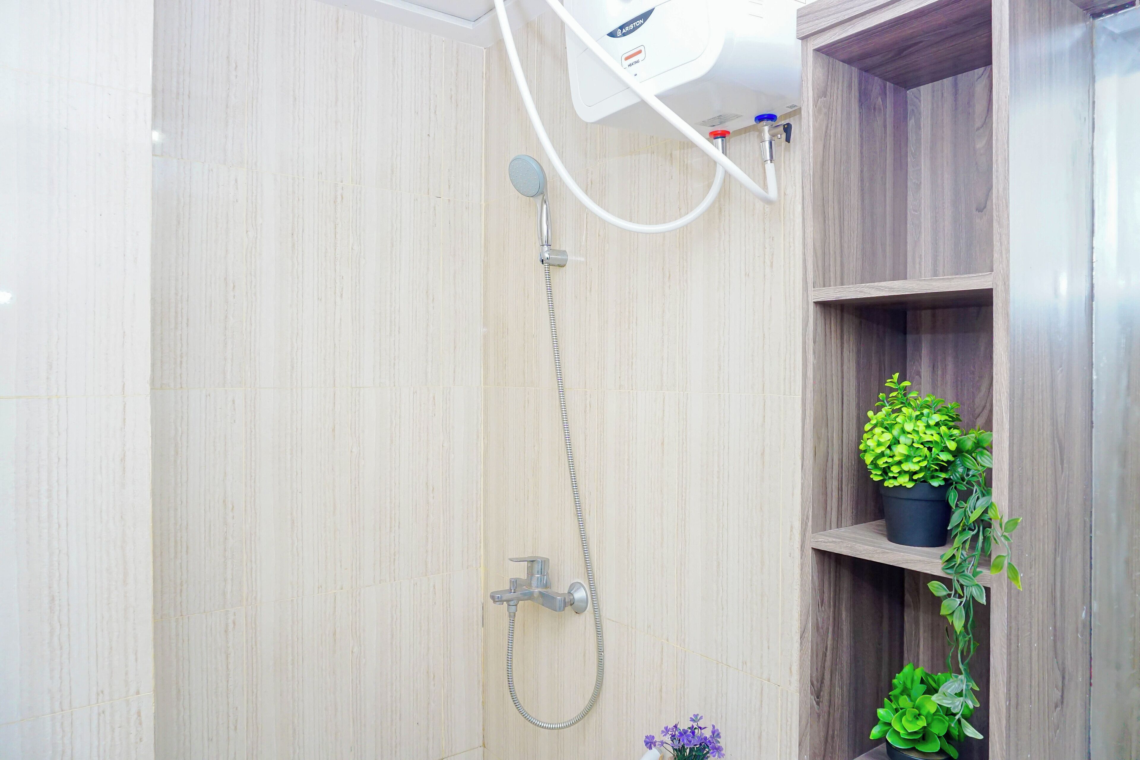 A shower with a handheld showerhead and a wall-mounted faucet. There are two potted plants on a wooden shelf.