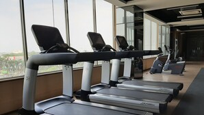 A row of treadmills in a gym with large windows and a view of buildings outside. - Fully Furnished with Cozy Design Studio Springwood Residence Tangerang Apartment (Tangerang)