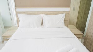 Un lit bien fait, avec du linge de lit blanc et deux oreillers, une tête de lit en bois et une armoire en bois sur le côté droit.