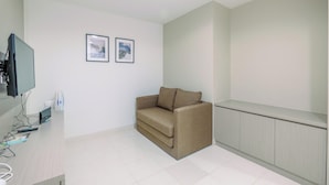 Een kamer met een beige bank, een flatscreen televisie en twee ingelijste foto’s aan de muur.