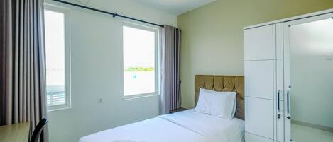 A hotel room with a bed, a wardrobe, a desk, and an air conditioning unit.