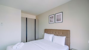Een net opgemaakt bed met witte lakens en kussens, een houten hoofdbord, en twee ingelijste foto's aan de muur.