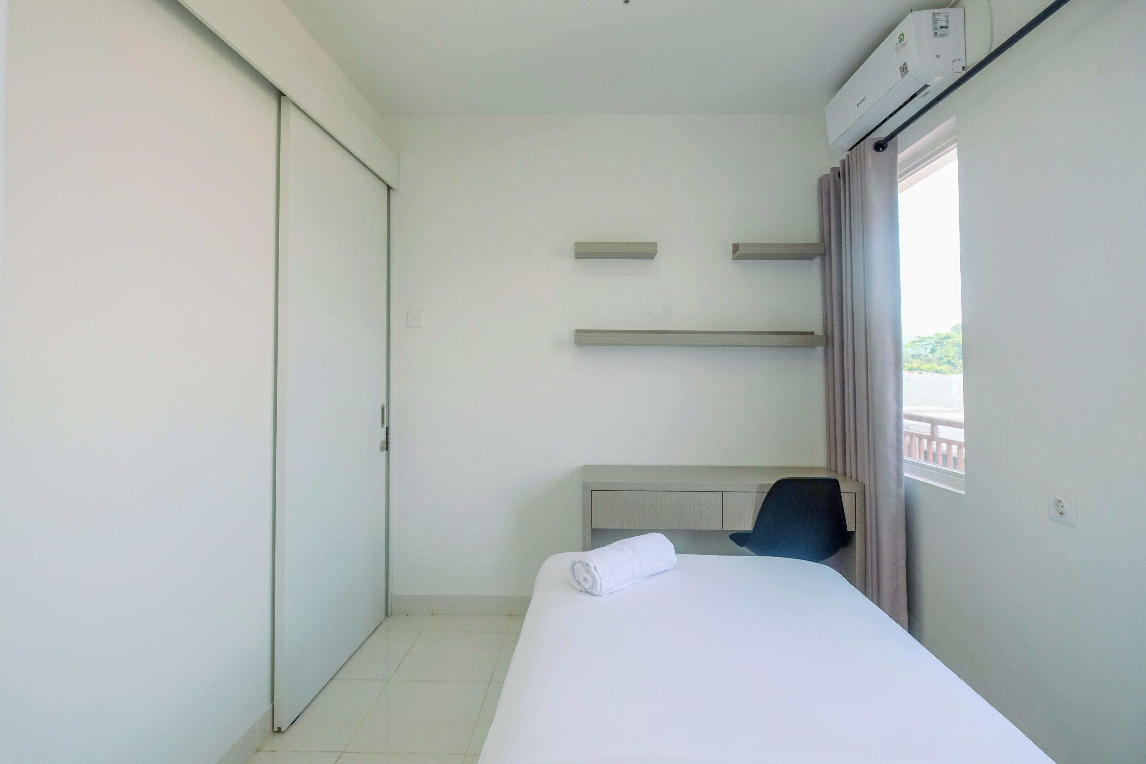 A hotel room with a bed, a desk, a chair, a wardrobe, and a window with curtains.