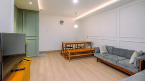 A living room with a wooden table, bench, grey sofa, and a television. - Modern Look 2BR at Sentul Tower Apartment (Citaringgul)