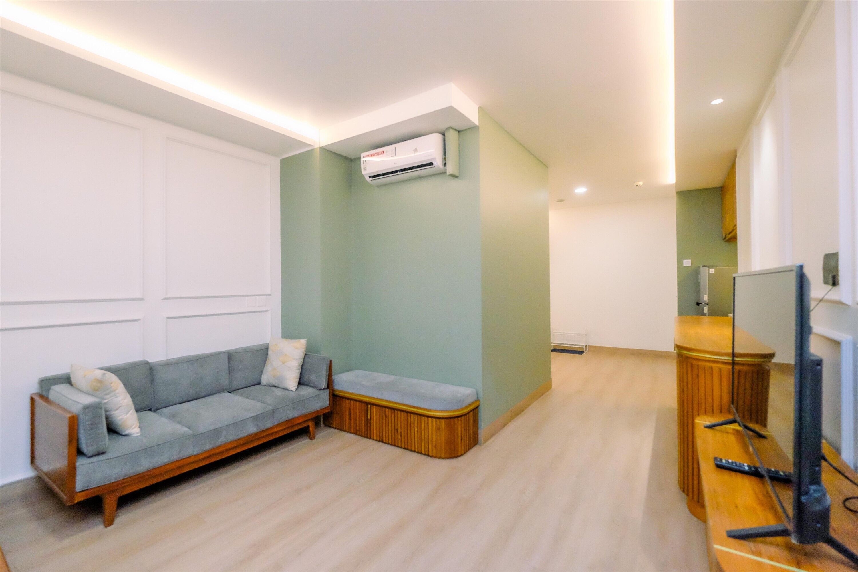 Una sala de estar con un sofá, un banco de madera, un televisor y un equipo de aire acondicionado.