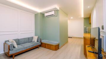 Una sala de estar con un sofá, un banco de madera, un televisor y un equipo de aire acondicionado.