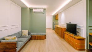 A modern living room with a grey sofa, wooden cabinet, and a flat-screen TV. - Modern Look 2BR at Sentul Tower Apartment (Citaringgul)