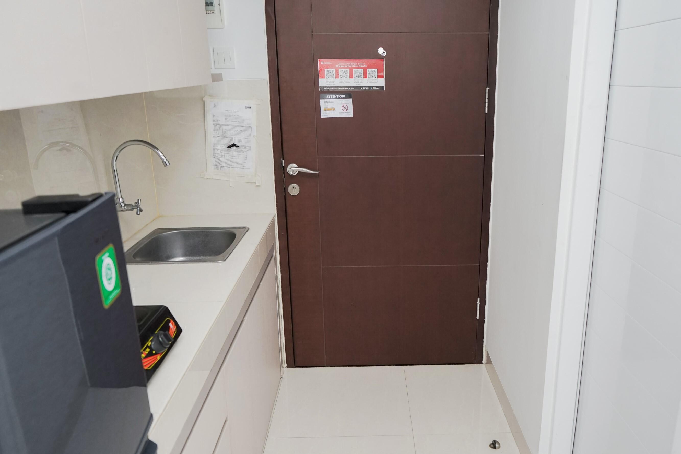 A small kitchen with a sink, a refrigerator, and a brown door with safety signs.