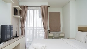 A hotel room with a bed, a desk with a computer, a TV, and a window with curtains.