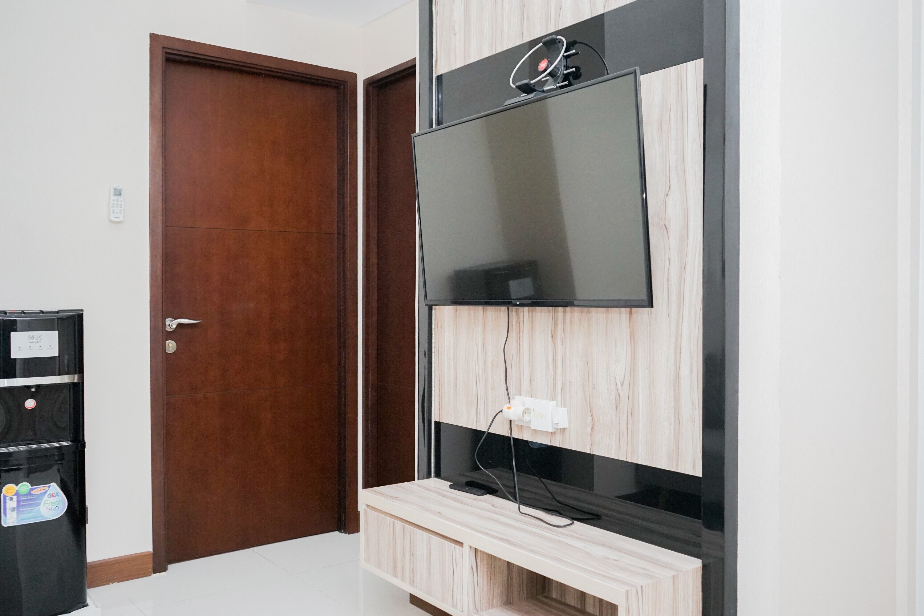 A room with a wooden door, a black refrigerator, and a wall-mounted TV.