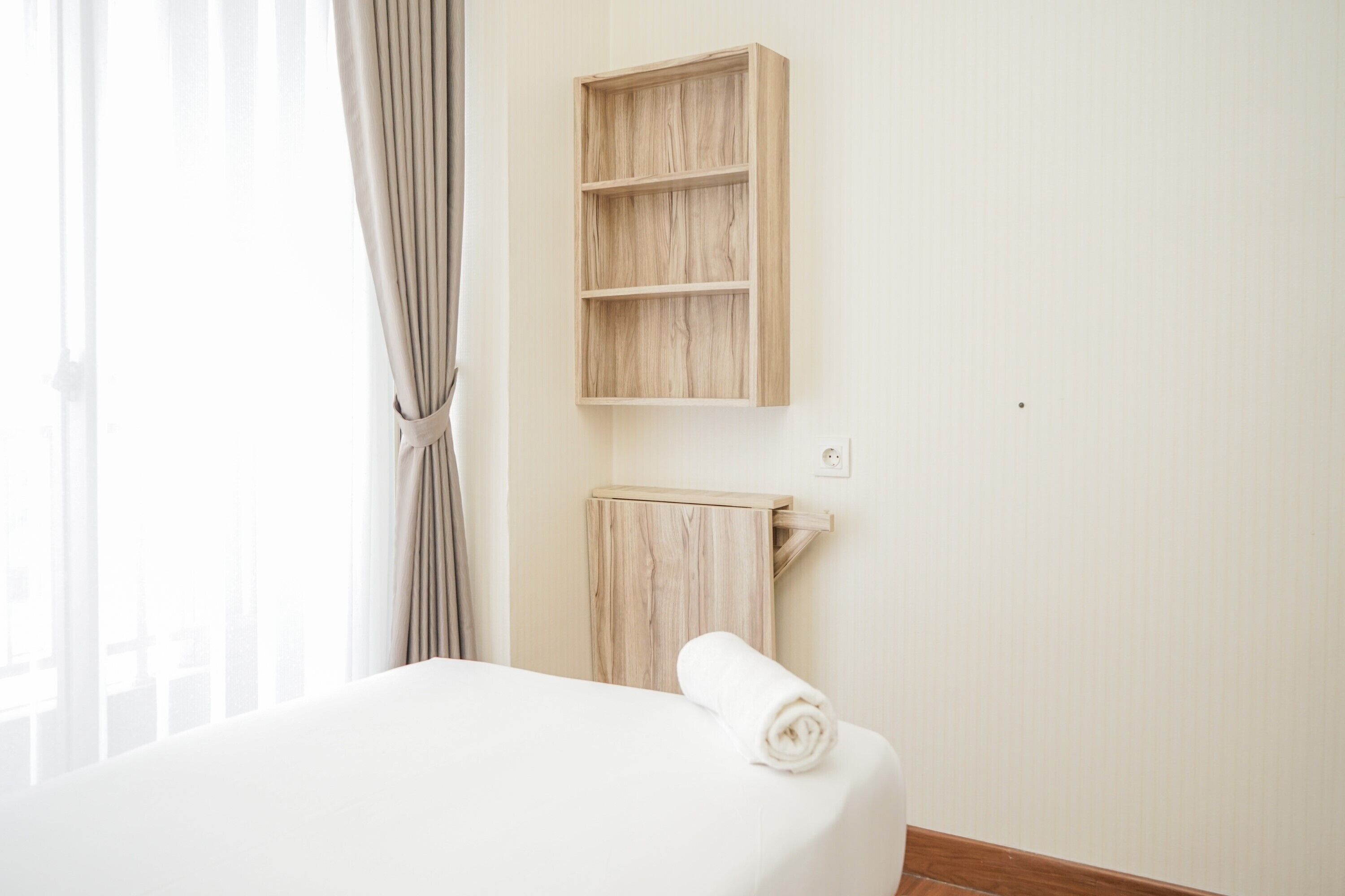 Une chambre d’hôtel avec un grand lit, une étagère en bois et une serviette posée sur le lit.