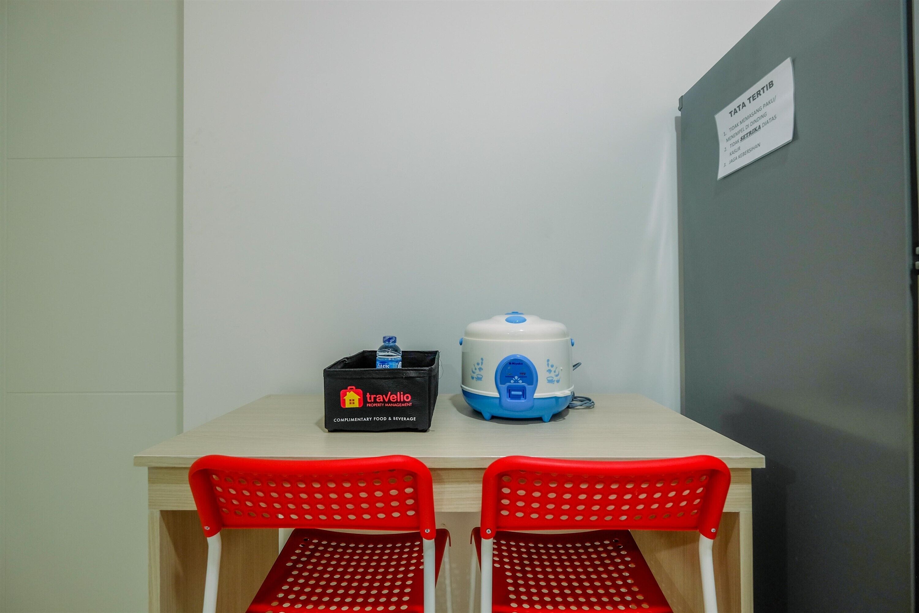 A small table with two red chairs, a water bottle, a travel bag, and a rice cooker.