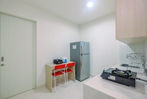 Una cocina compacta con refrigerador, una pequeña mesa con dos sillas rojas, estufa portátil y lavamanos.