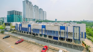 A modern building with a blue and white facade, surrounded by a parking area with several cars. - Homey 2BR at Sentul Tower Apartment (Citaringgul)