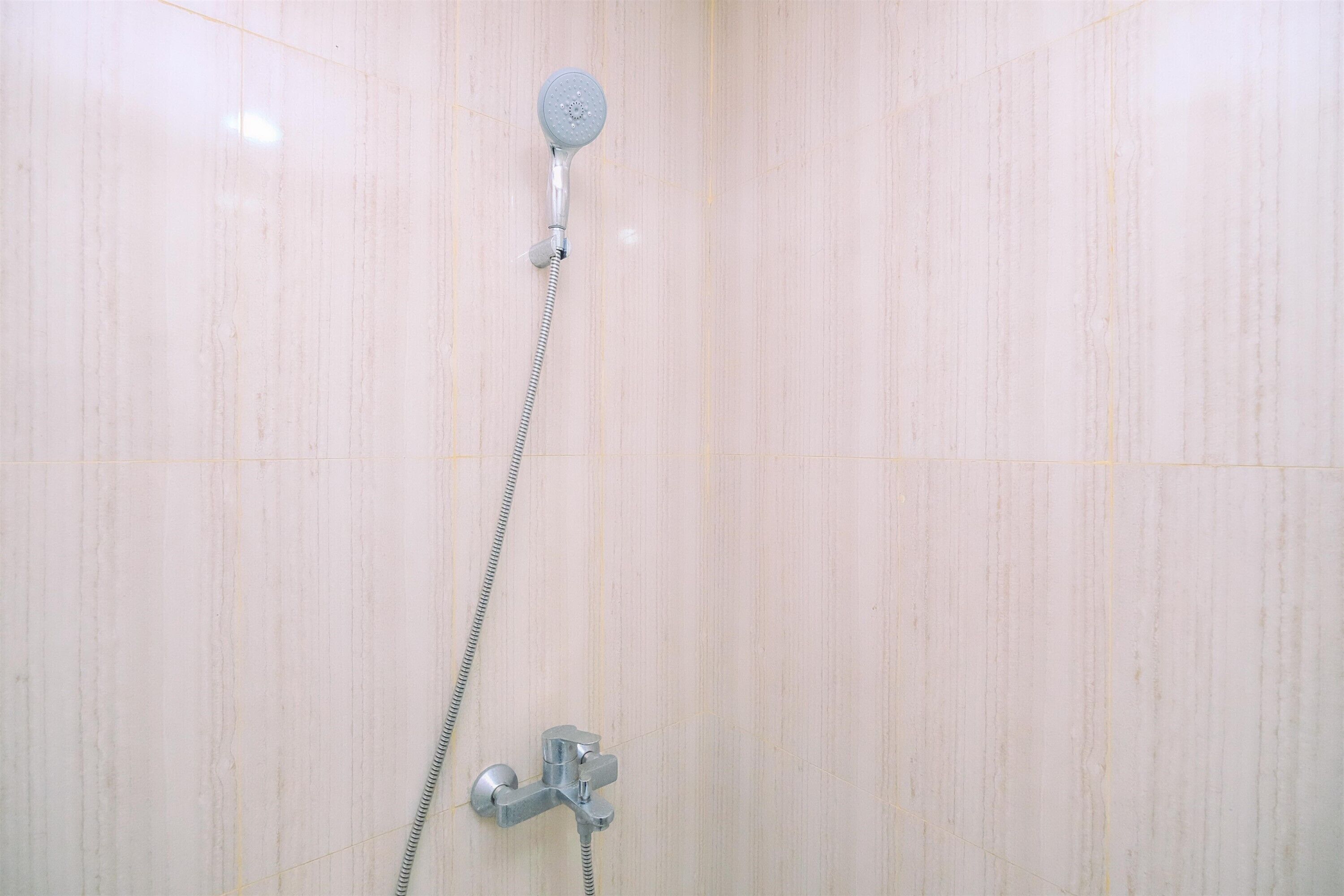 Une douche équipée d’un pommeau de douche à main et d’un robinet fixé au mur.