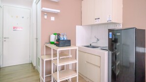 A compact kitchen with a refrigerator, sink, and a small table with a water dispenser. - Cool and Warm Studio at Sentul Tower Apartment (Citaringgul)