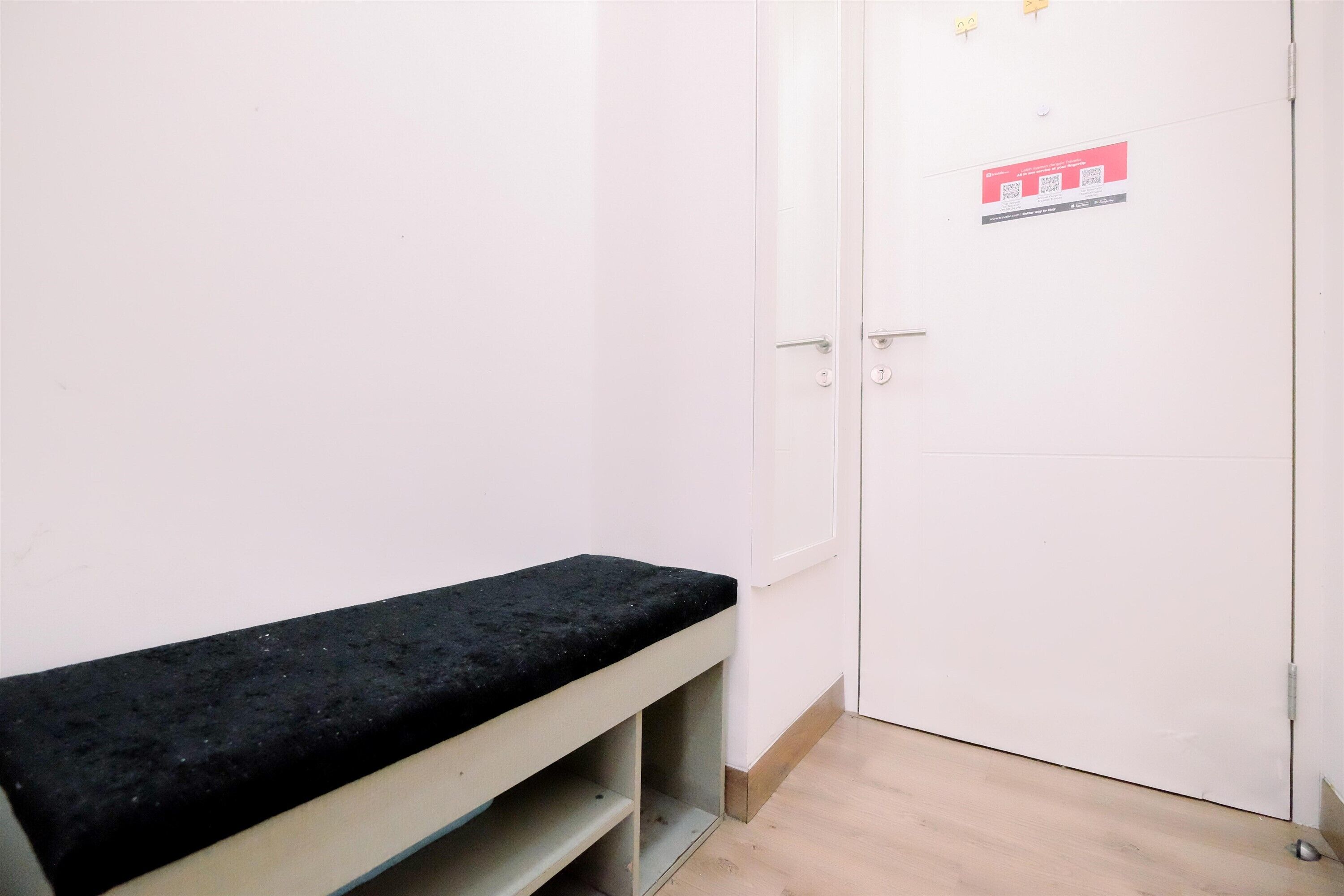 Une pièce avec un banc, une porte blanche ornée d’un logo rouge et un plancher en bois clair.
