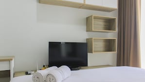 A hotel room with a bed, a flat-screen TV, wooden shelves, and a window with curtains.