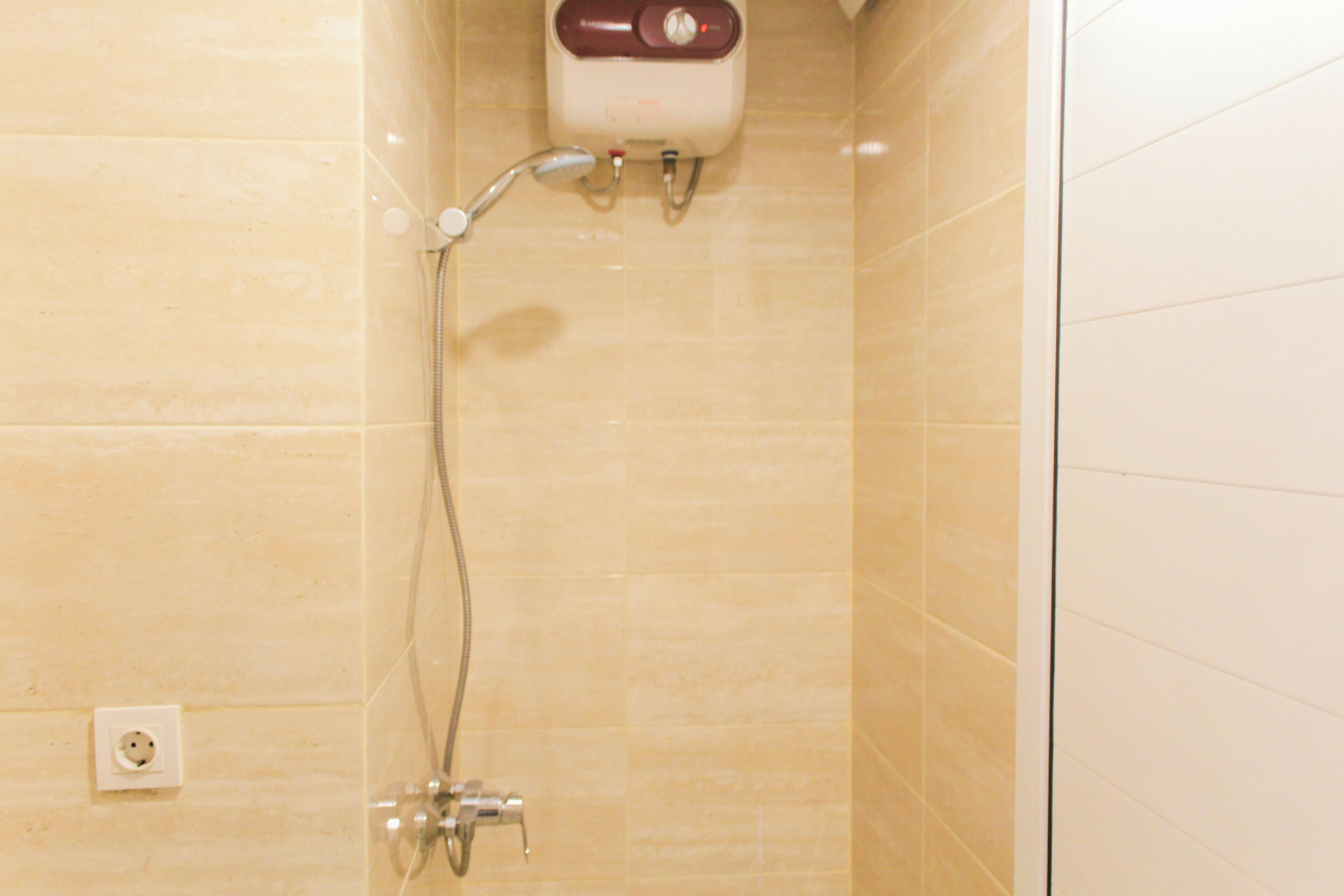 A bathroom with beige tiles, a shower with a handheld showerhead, and a wall-mounted control panel.