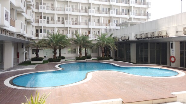 A modern apartment building with a central swimming pool, surrounded by palm trees and a well-maintained courtyard. - Relax 1BR Apartment at Sentul Tower (Citaringgul)